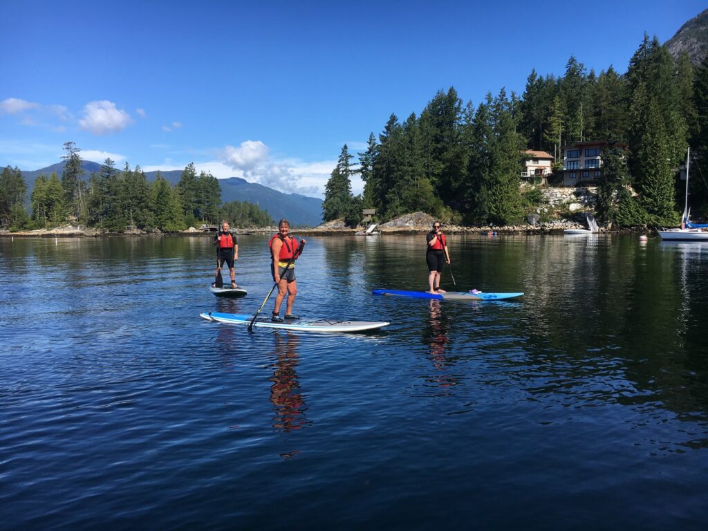 three individuals each standing on a paddle board on the calm waters of the Sechelt Inlet.